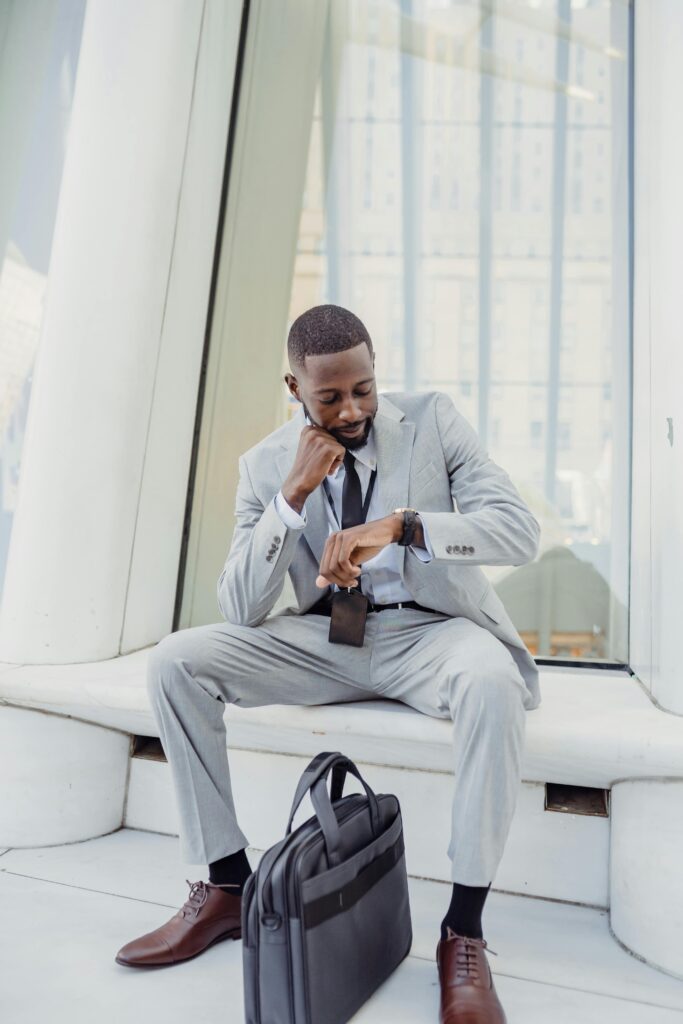 Professional businessman in a suit checking his wristwatch indoors with a laptop bag nearby.
