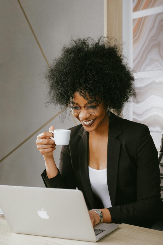 African American woman enjoying coffee while working on a laptop indoors.